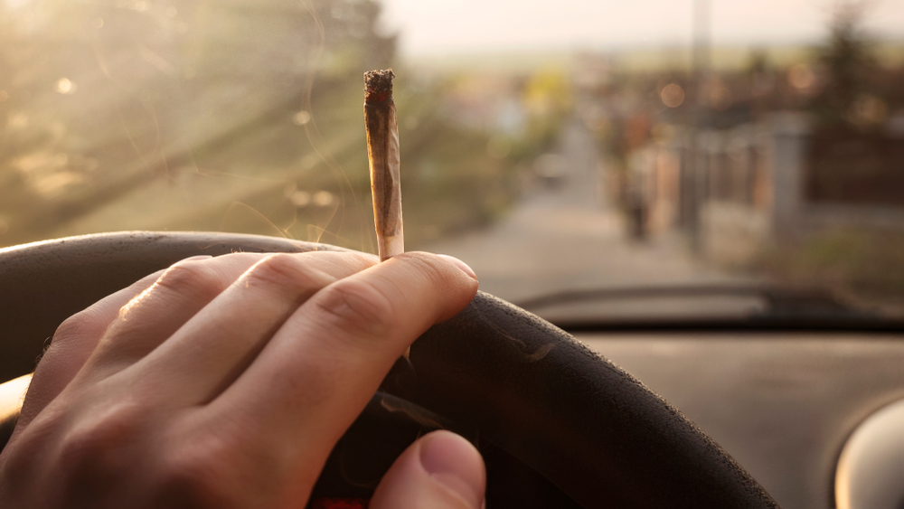 une main tenant un volant et un joint de cannabis