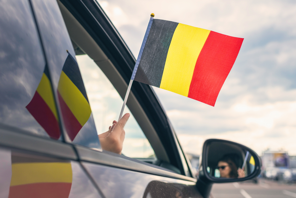 main d'une femme qui tient un drapeau de la Belgique à travers la fenêtre de la voiture