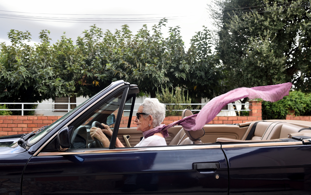 femme âgée avec une écharpe au vent et les cheveux coupés courts blancs dans un véhicule décapotable