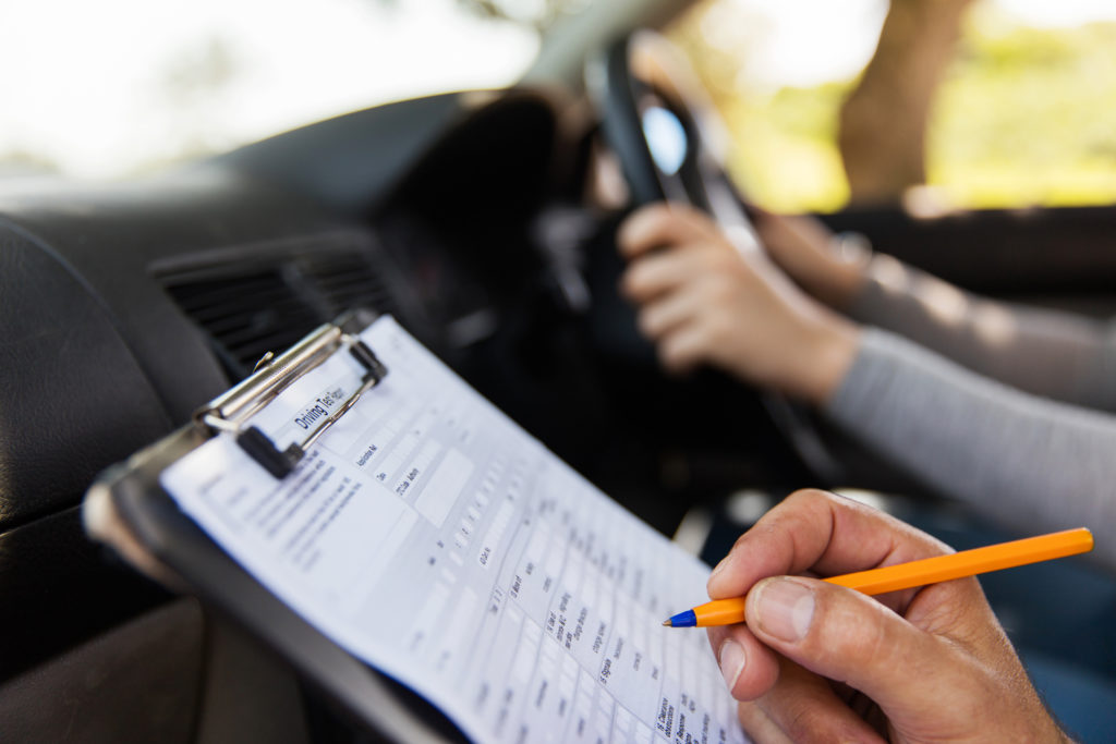 gros plan sur fiche d'examen. Une main tenant un stylo note sur la fiche d'examen avec les 2 bras floutés d'une personne tenant le voalnt en arrière plan