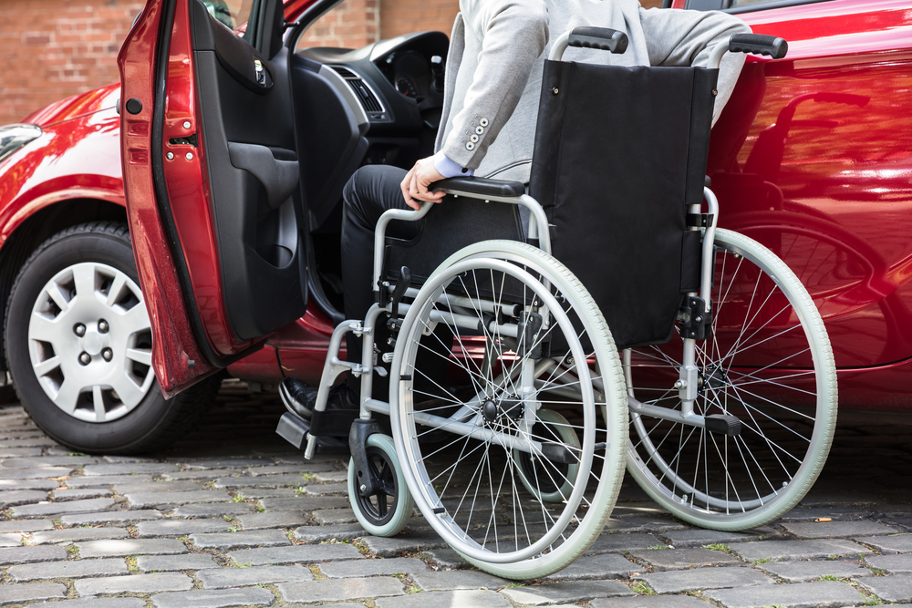un homme assis dans un fauteuil roulant monte dans sa voiture rouge